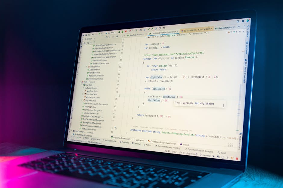 A close-up of a laptop displaying lines of computer code with syntax highlighting, set against a dark background illuminated by pink and blue ambient lighting. The screen shows a programming environme